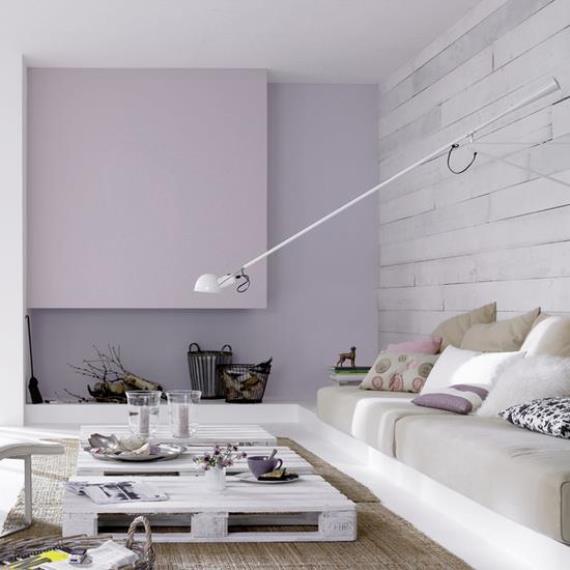 Καθιστικό με μοντέρνο design σε λευκές και υπόλευκες αποχρώσεις. Το λιλά στον τοίχο και η φωτεινότερη απόχρωση στο τζάκι ενισχύει την αισθητική του χώρου.