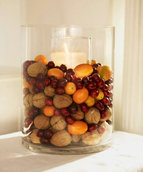 Ένα διάφανο βάζο με κερί γεμάτο με καρύδια, κουμκουάτ και κράνμπερι.